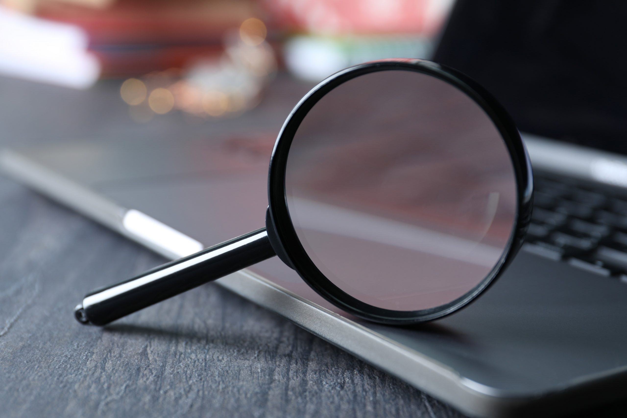 Magnifying glass on laptop keyboard on wooden background, close